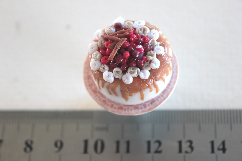 Iced cake topped with berries and cinnamon sticks with caramel drizzle, on a cake stand in 1/12 scale miniature