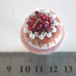 Iced cake topped with berries and cinnamon sticks with caramel drizzle, on a cake stand in 1/12 scale miniature